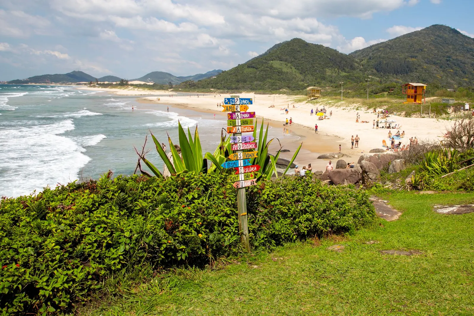 Placa colorida na praia com morros ao fundo, em Garopaba